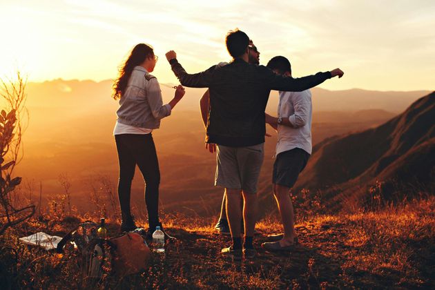 Friends on a mountaintop at sunset, arms raised in celebration. Orange light illuminates the scene.