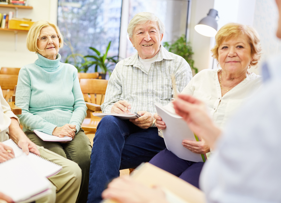 A group of elderly people are sitting in a circle holding papers.