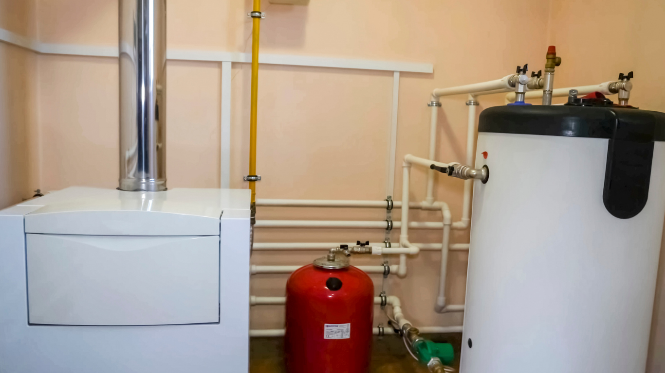 White heating unit and water tank with connected pipes in a room. Red expansion tank.