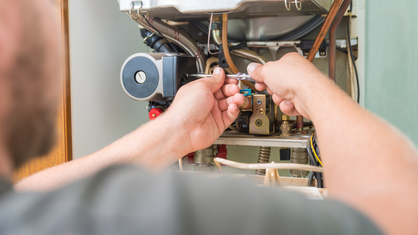 A person repairs a heating system with tools, near electrical and plumbing components.