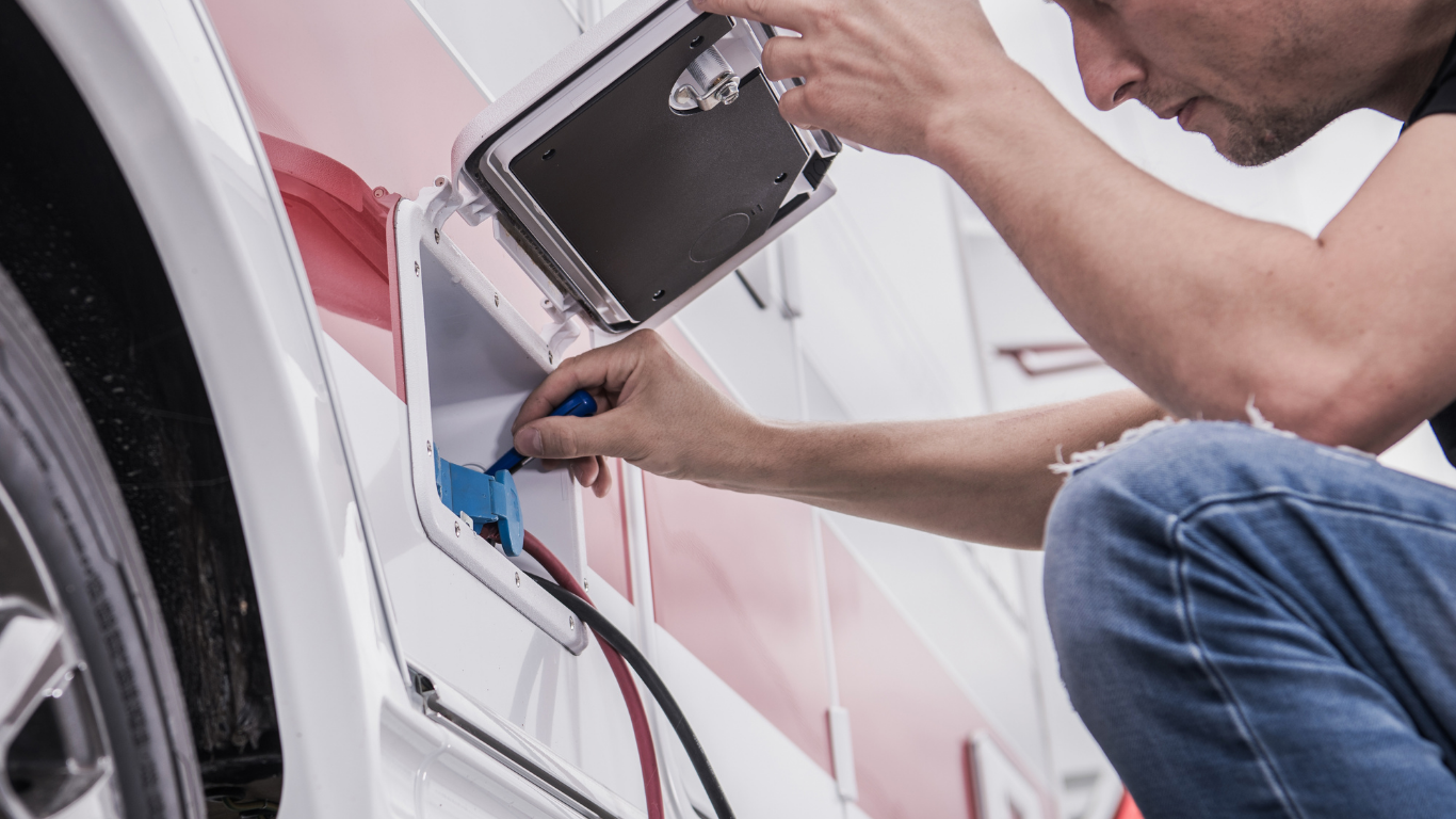 Man connecting RV electrical cord to the side of a camper.