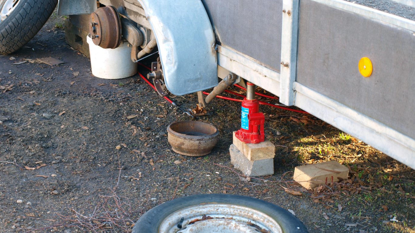 A trailer being repaired, with a jack propping it up and the wheel off.