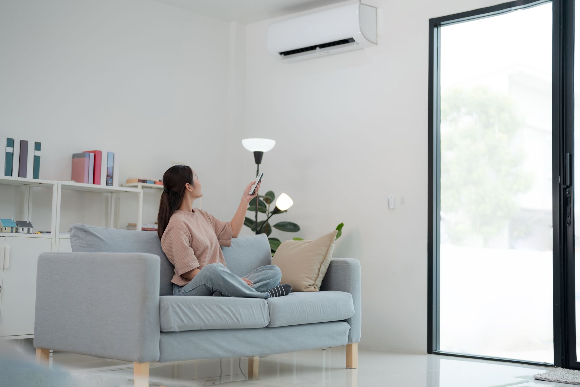 A woman is sitting on a couch in a living room holding a remote control.