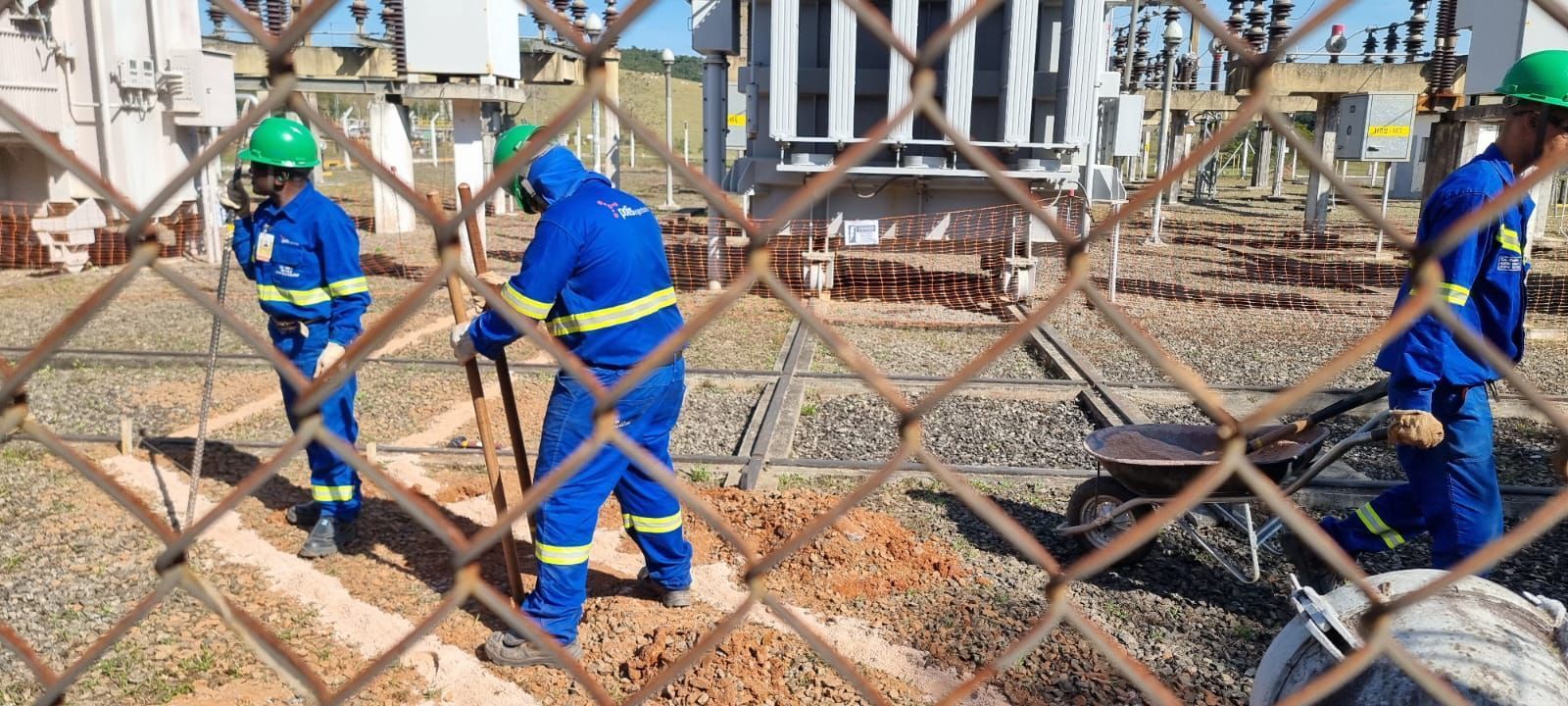 Um grupo de trabalhadores da construção civil está trabalhando em um campo atrás de uma cerca de arame.