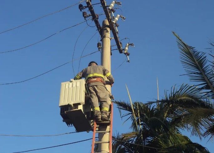 Um homem em uma escada está trabalhando em um poste elétrico