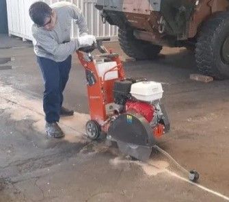Um homem está usando uma serra de concreto para cortar um buraco no chão.