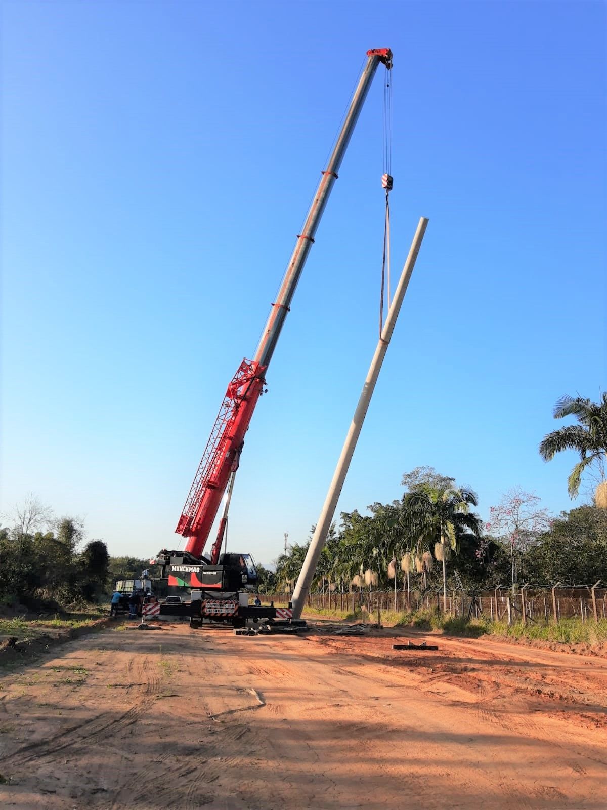 Um guindaste vermelho está levantando um poste em um campo de terra