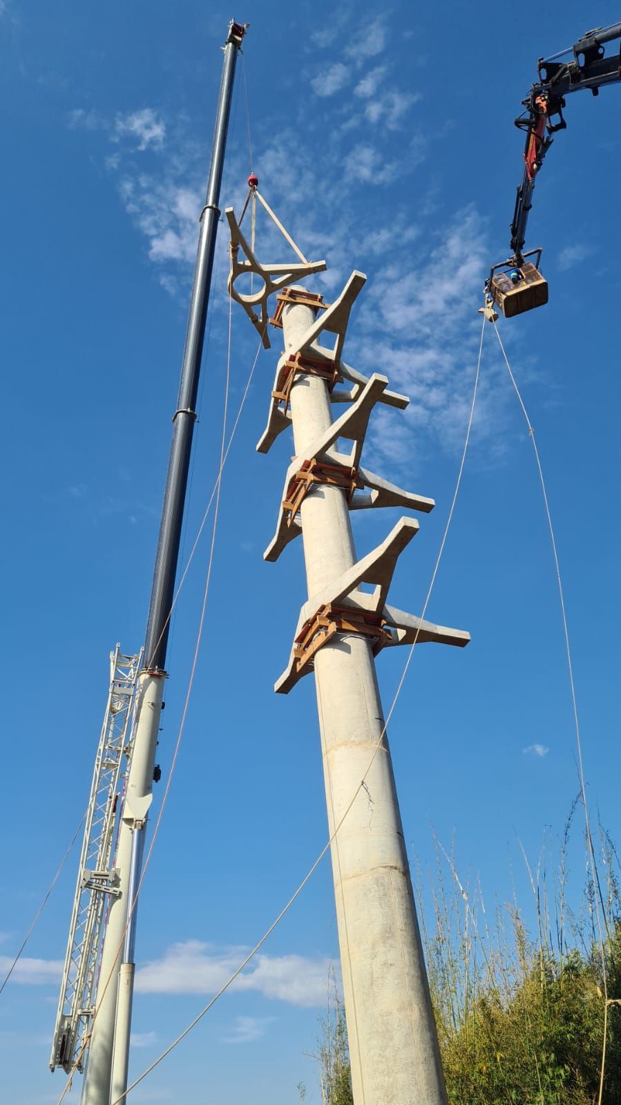 Um guindaste está levantando um poste de concreto com uma escada presa a ele.