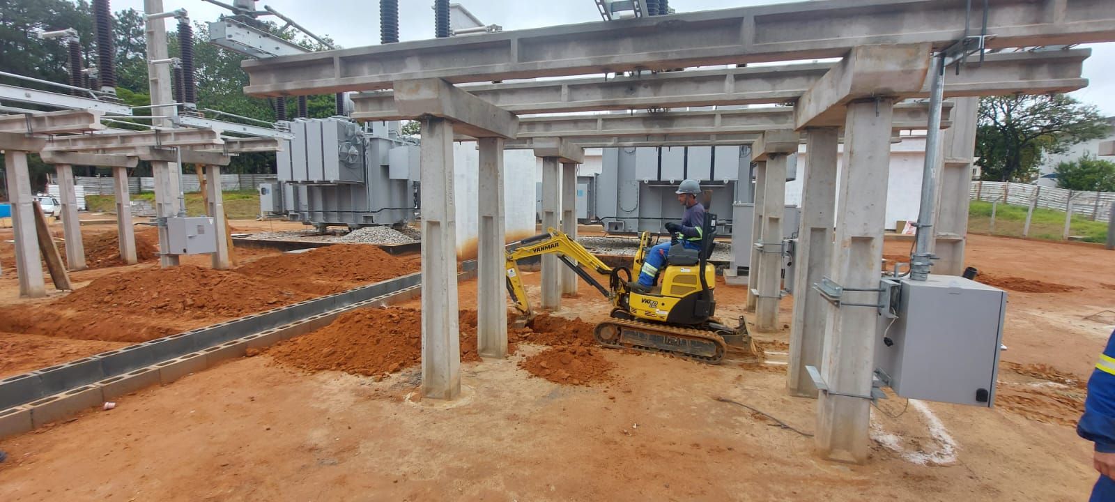 Uma escavadeira amarela está parada na terra em frente a um prédio em construção.