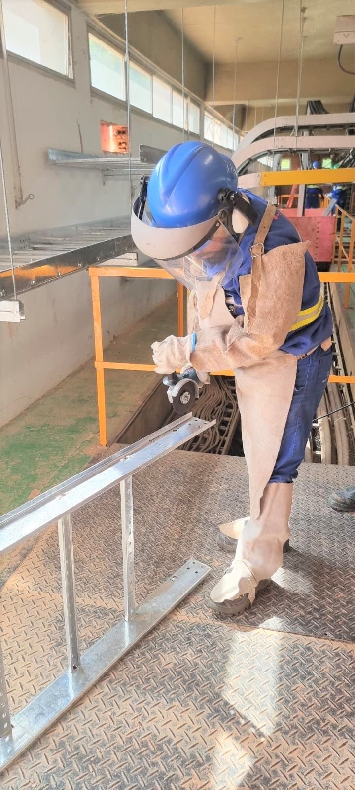 Um homem usando capacete e óculos de segurança está trabalhando em um corrimão em uma fábrica.