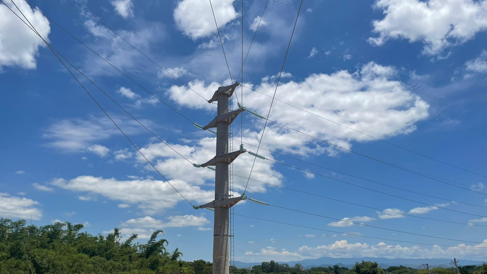 Um poste telefônico com um céu azul e nuvens brancas ao fundo.
