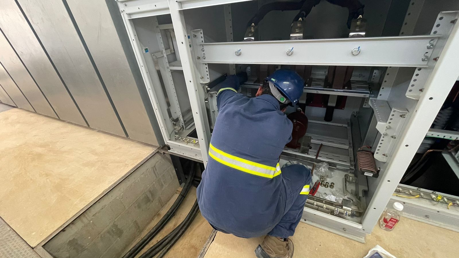 Um homem de macacão azul está trabalhando em uma caixa elétrica.