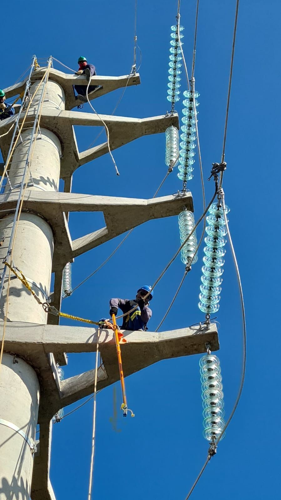 Um homem está trabalhando em uma linha de energia no topo de uma torre de concreto.