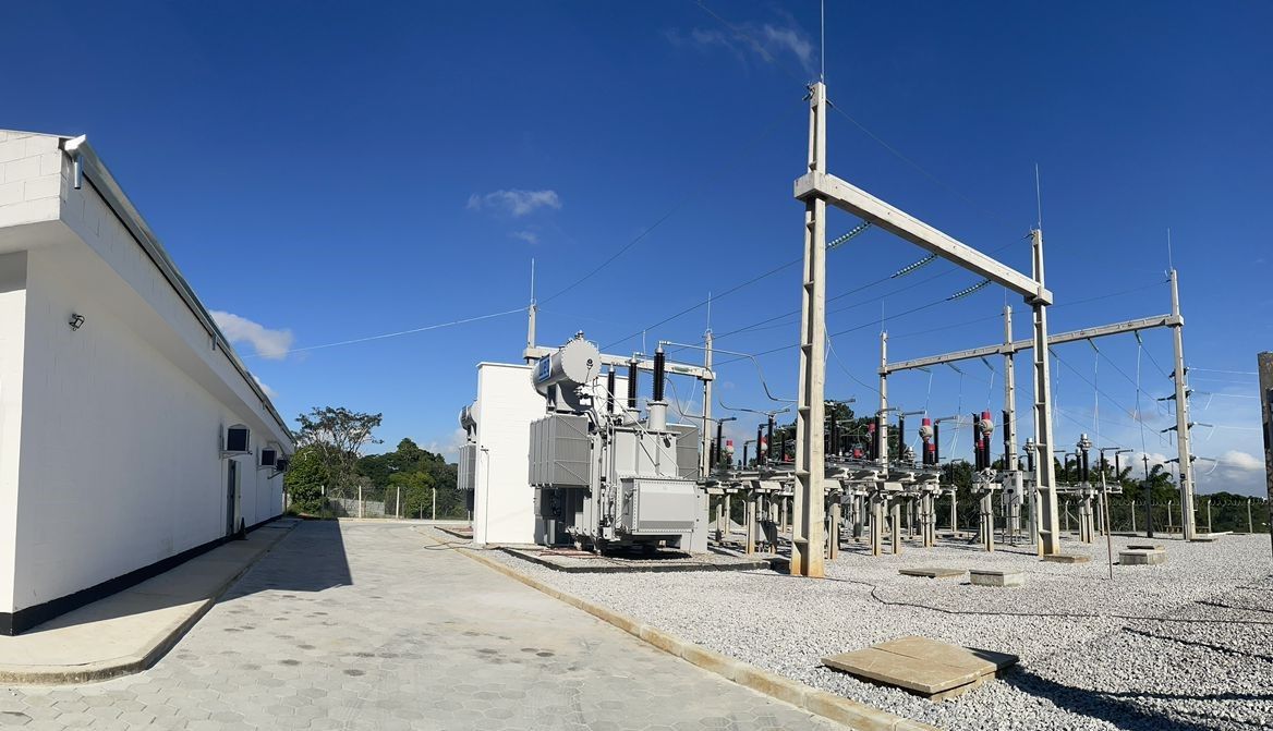 Uma usina elétrica com muitos transformadores e um prédio ao fundo.