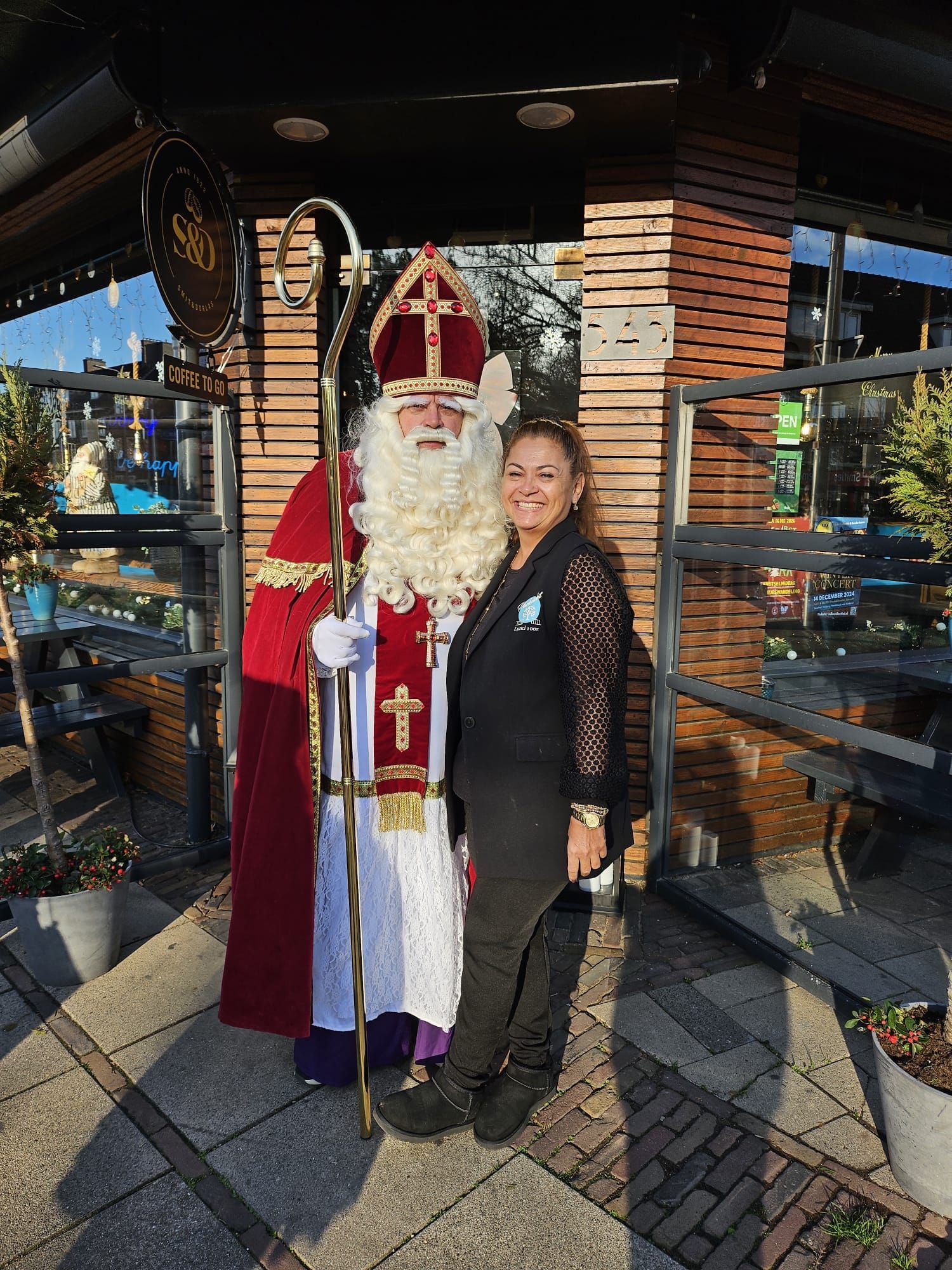 Een man verkleed als Sinterklaas poseert samen met een vrouw in de buitenlucht.