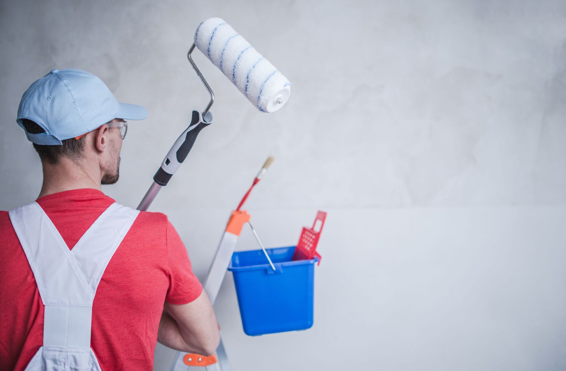 Painter with paint roller, brush, and bucket on a wall.