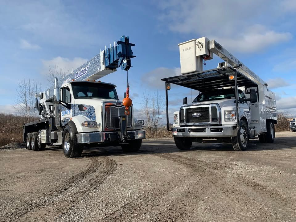 A white crane truck and a white bucket truck parked outdoors under a blue sky.