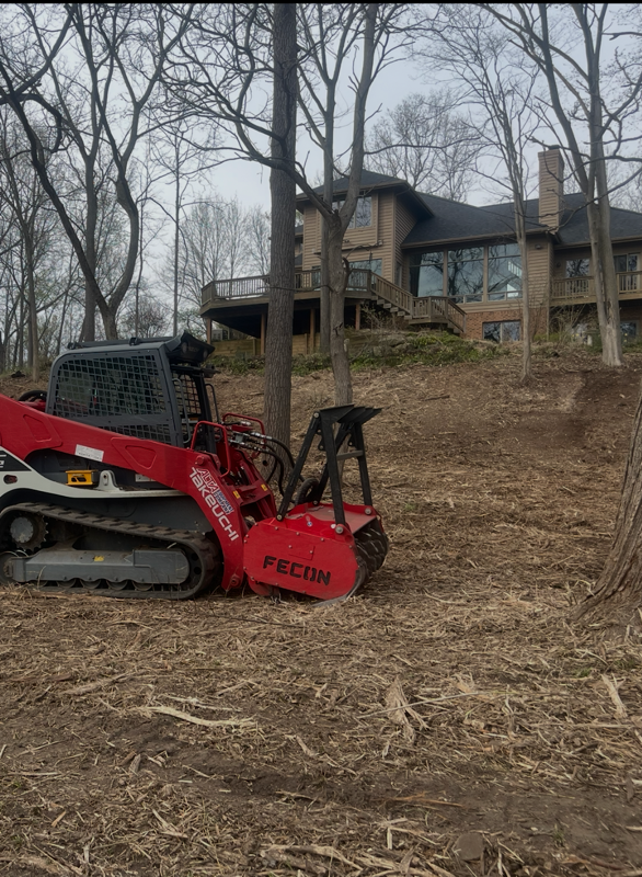Arborists trimming tree branches near a wood chipper, wearing safety vests and hard hats.
