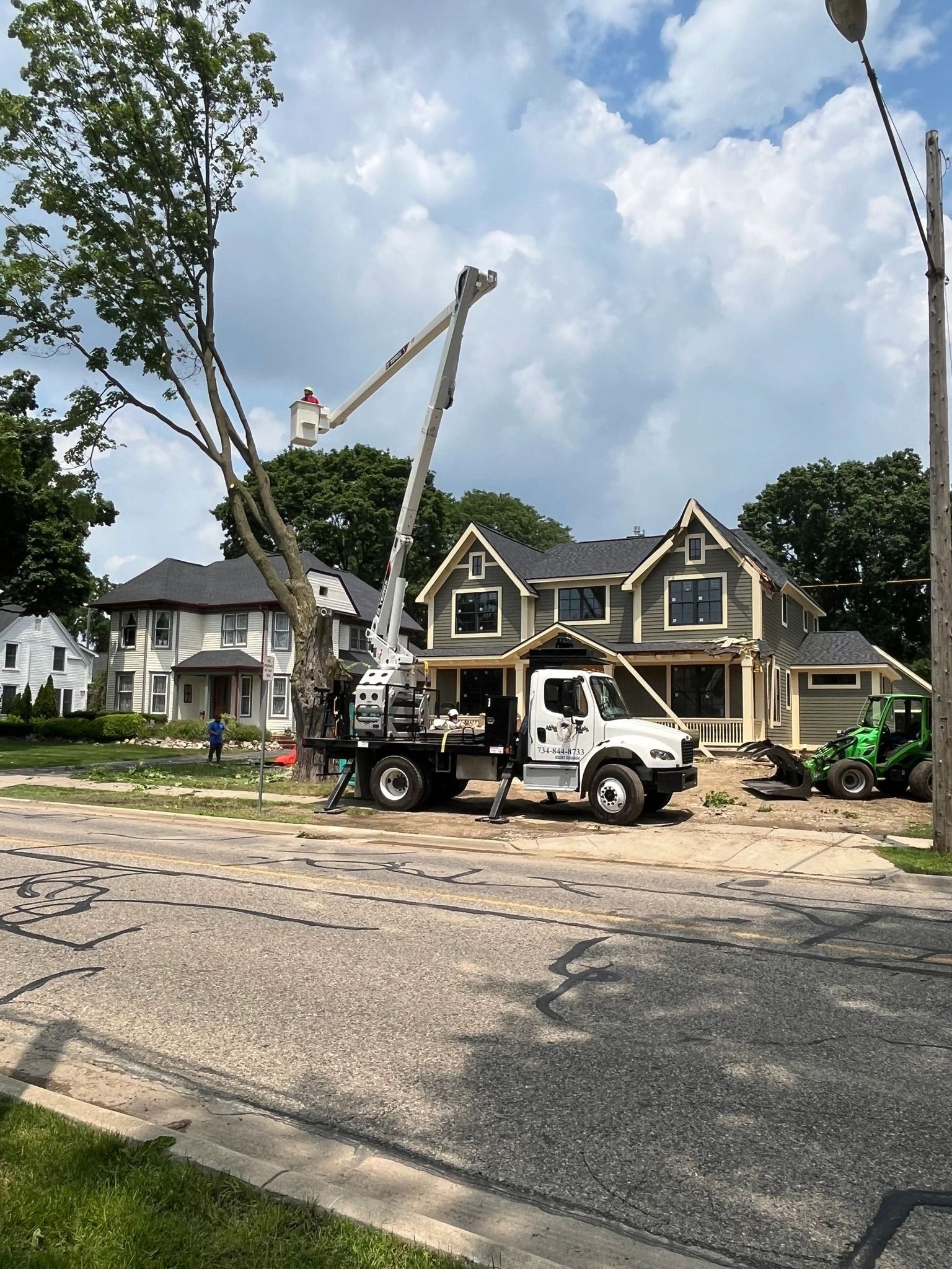 Truck with a crane trimming a tree in front of a house. Cloudy sky.