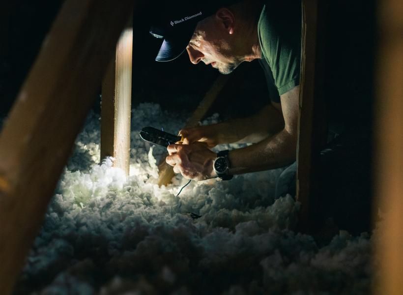 A man is working in an attic with a flashlight.