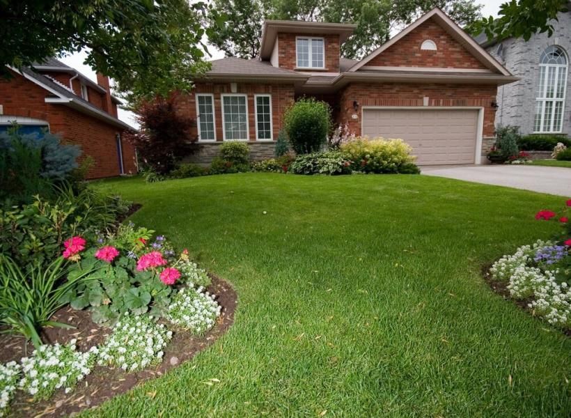 A house with a lush green lawn and flowers in front of it