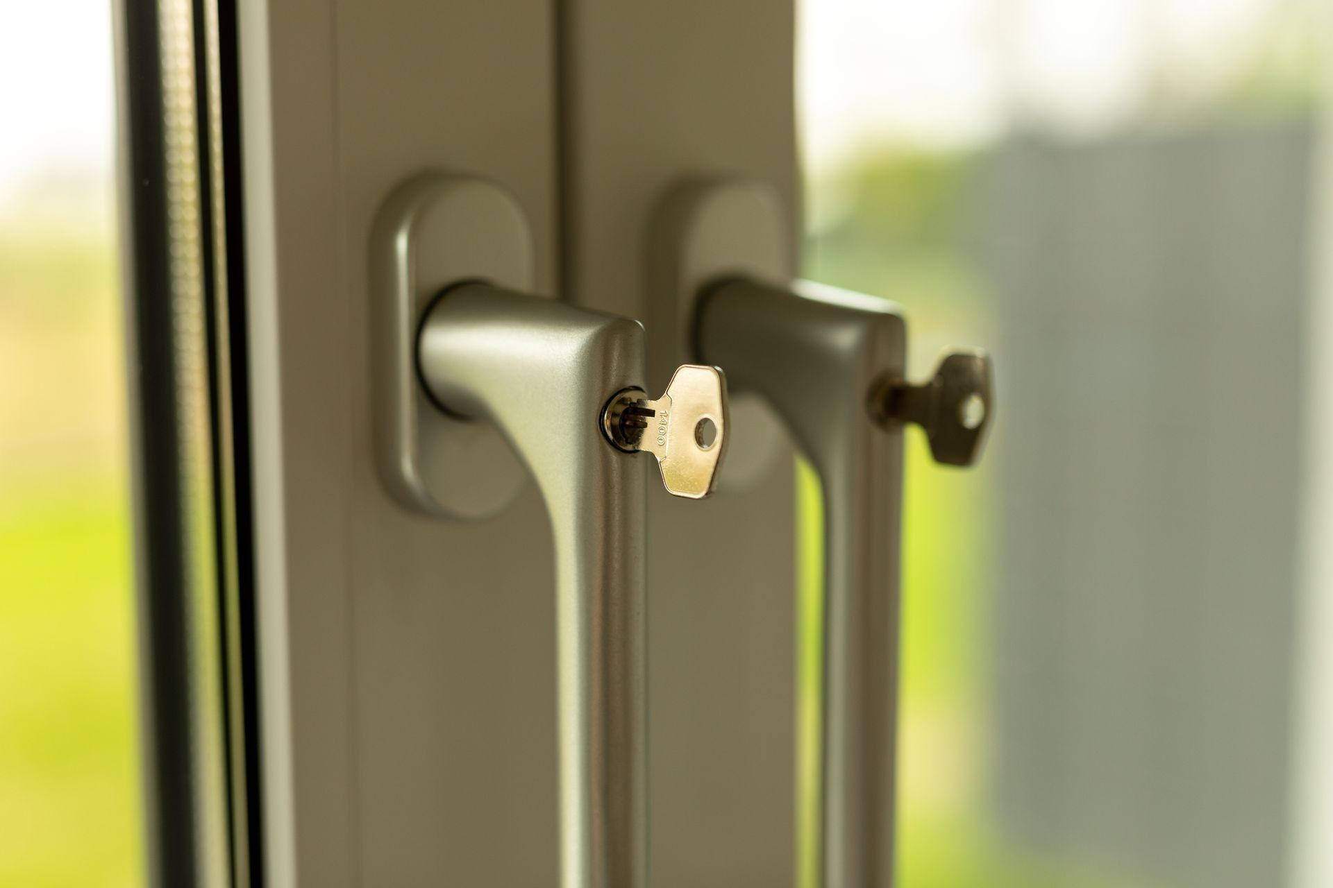 Two light-colored metal window handles with keys inserted into their lock mechanisms.