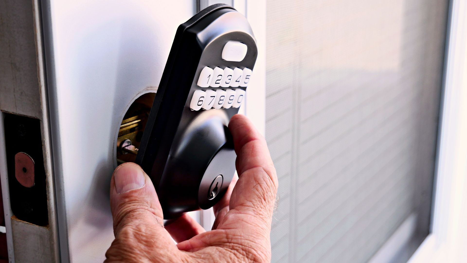A hand presses buttons on a black digital keypad lock installed on a light-colored door.