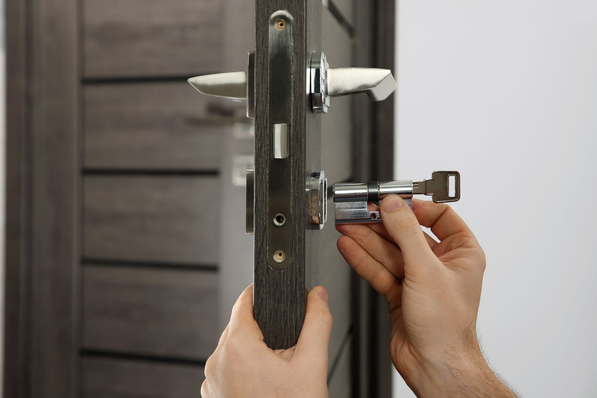 Hands inserting a silver door lock cylinder into a dark wood door.