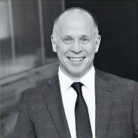 A man in a suit and tie is smiling in a black and white photo.