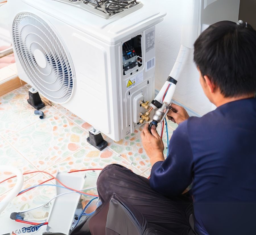 A man is sitting on the floor working on an air conditioner.