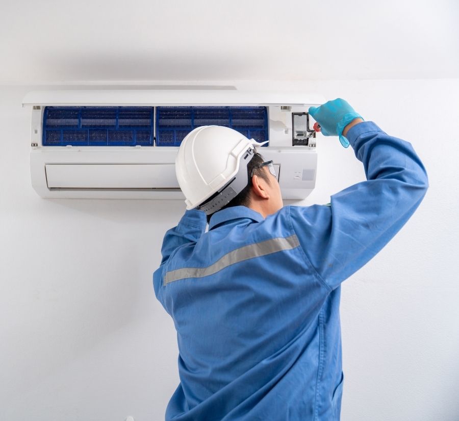 A man wearing a hard hat is working on an air conditioner.