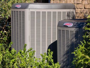 Two air conditioners are sitting next to each other on the side of a house.