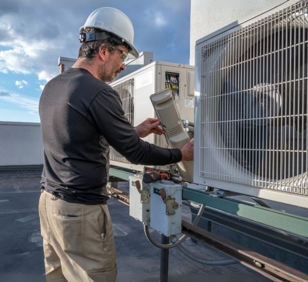 A man wearing a hard hat is working on an air conditioner