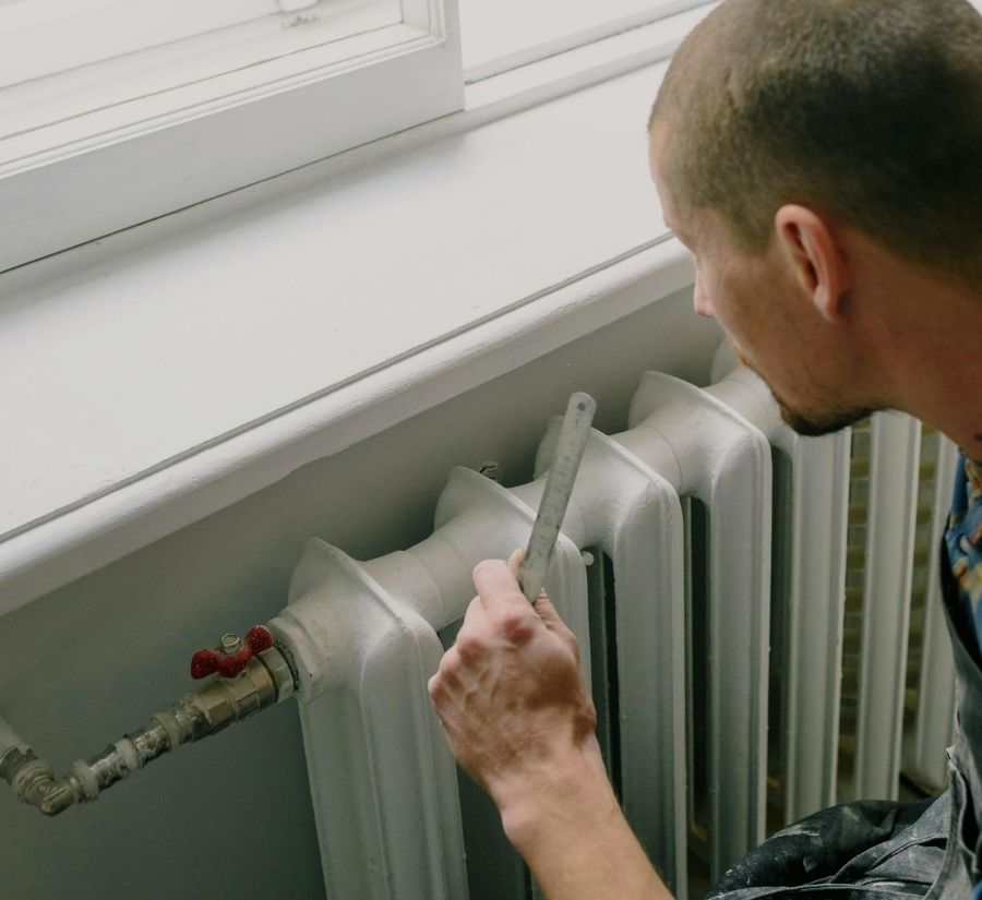 A man is measuring a radiator with a ruler