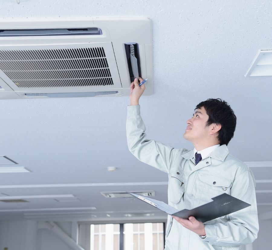 A man is working on an air conditioner while holding a clipboard.