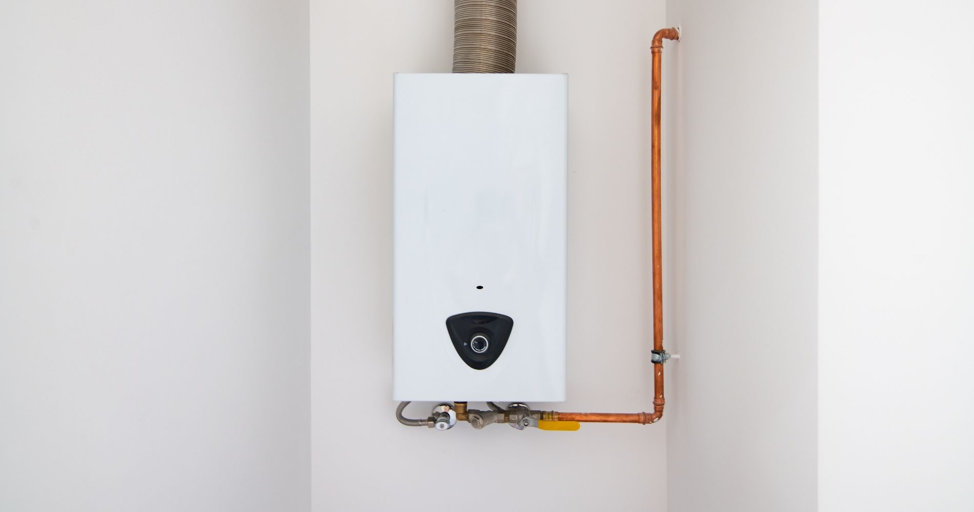 A white water heater is hanging on a white wall next to a copper pipe.