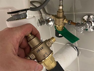 A person is holding a brass valve under a sink.