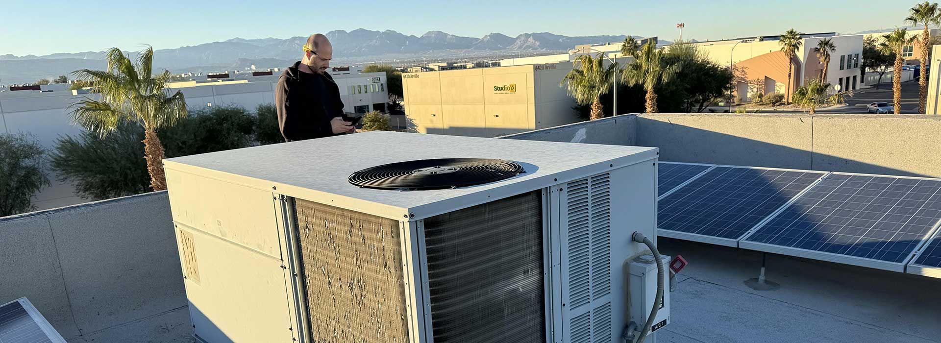 A man is standing on top of an air conditioner on a roof.