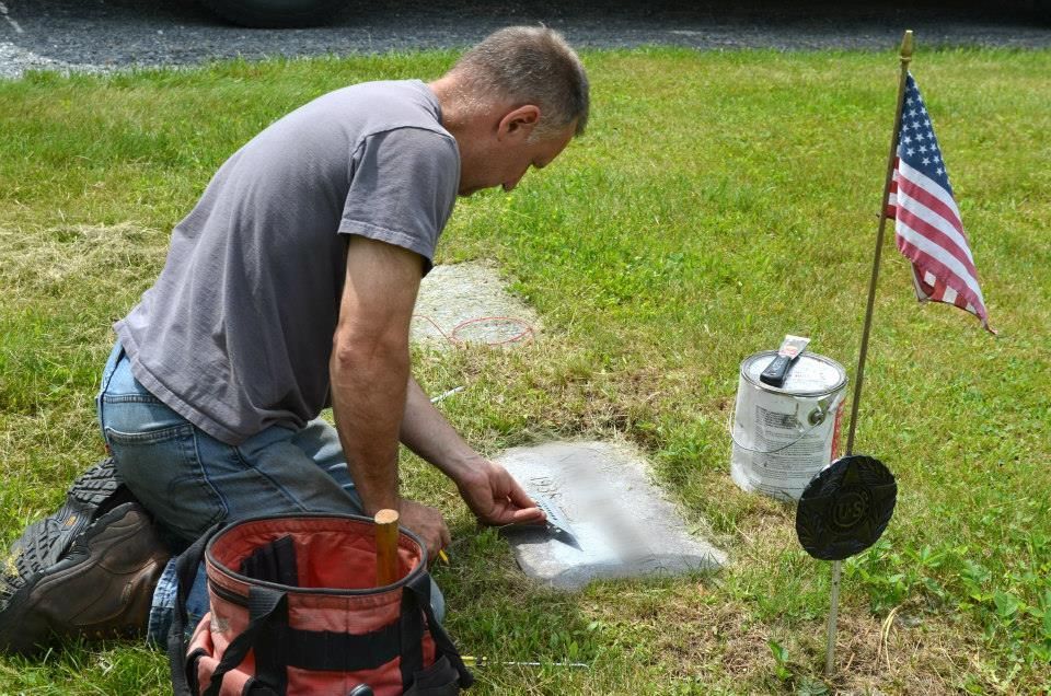 A large rock with a plaque on it is in the middle of a park next to a picnic table.