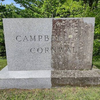 A large rock with a plaque on it is in the middle of a park next to a picnic table.