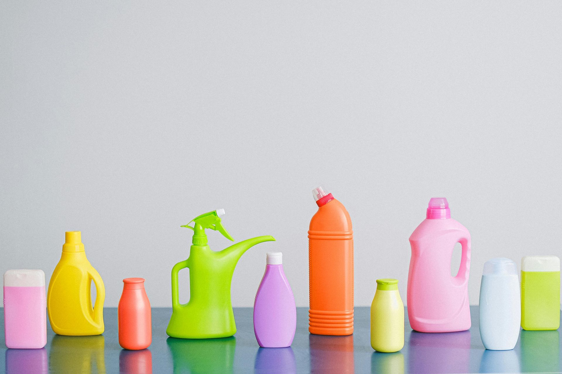 Row of colorful plastic cleaning product bottles on a reflective blue surface, against a plain white background.