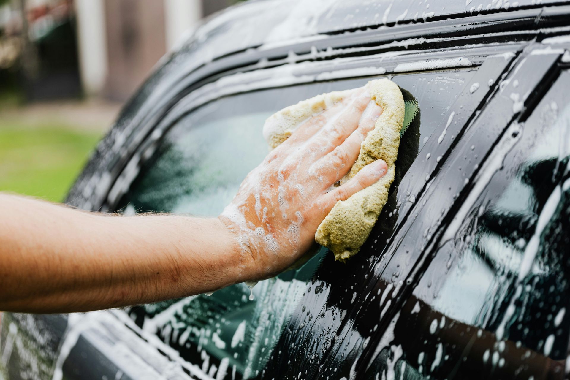 Person washing a car window with a soapy sponge outdoors.