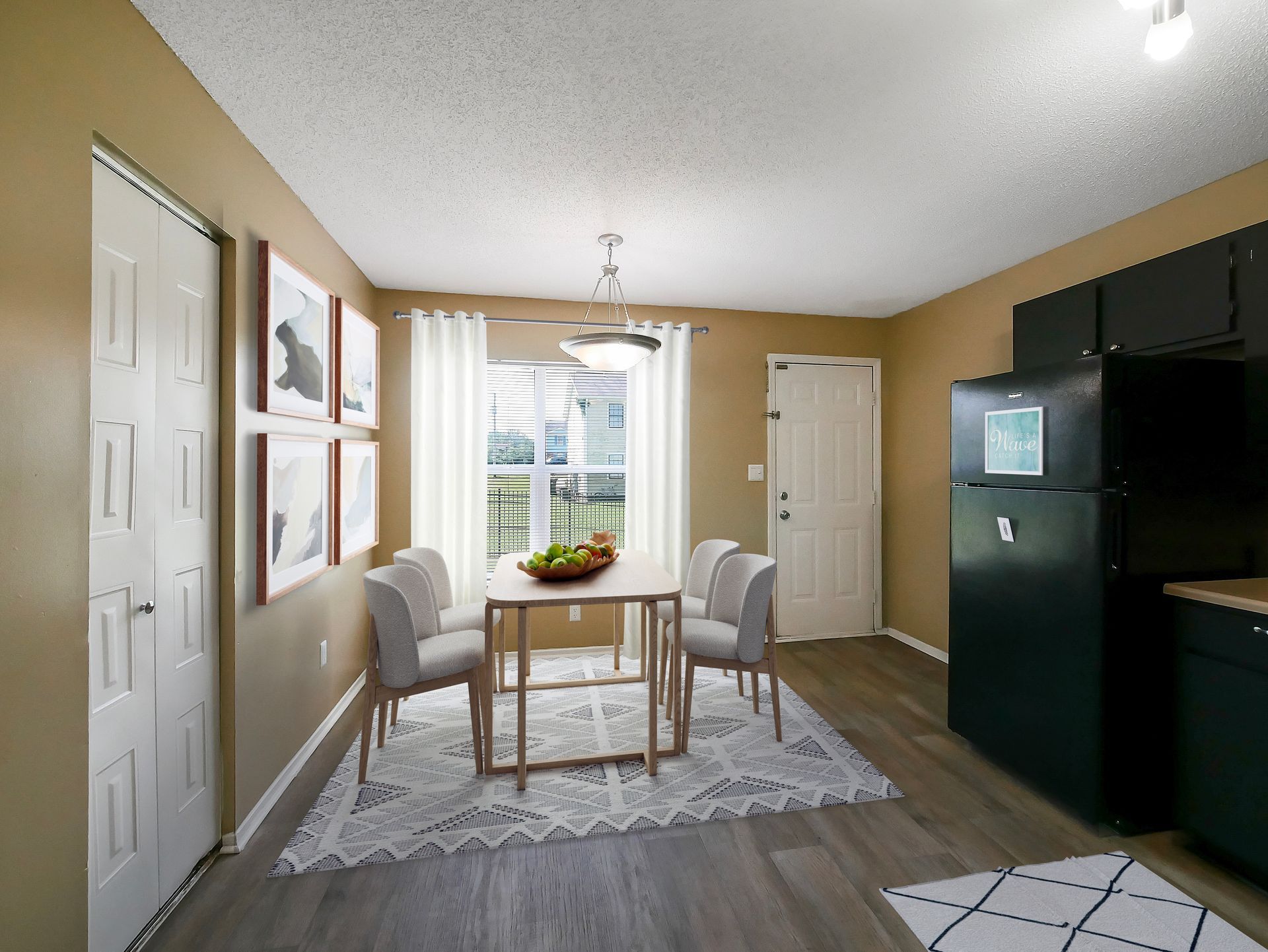 Dining area with a wooden table, four gray chairs, a patterned rug, a large black refrigerator, and a door.