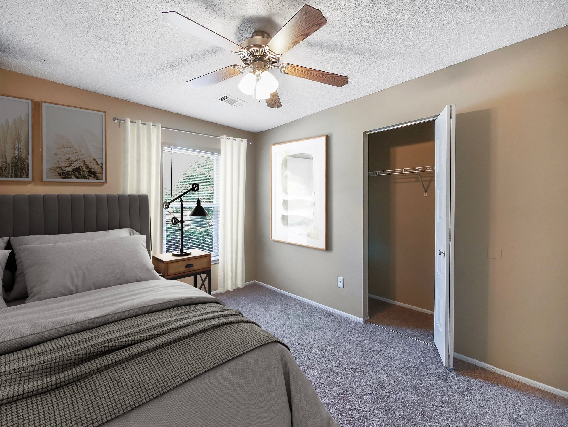 A bedroom with a gray tufted headboard, white curtains, a ceiling fan, framed wall art, and an open closet door.