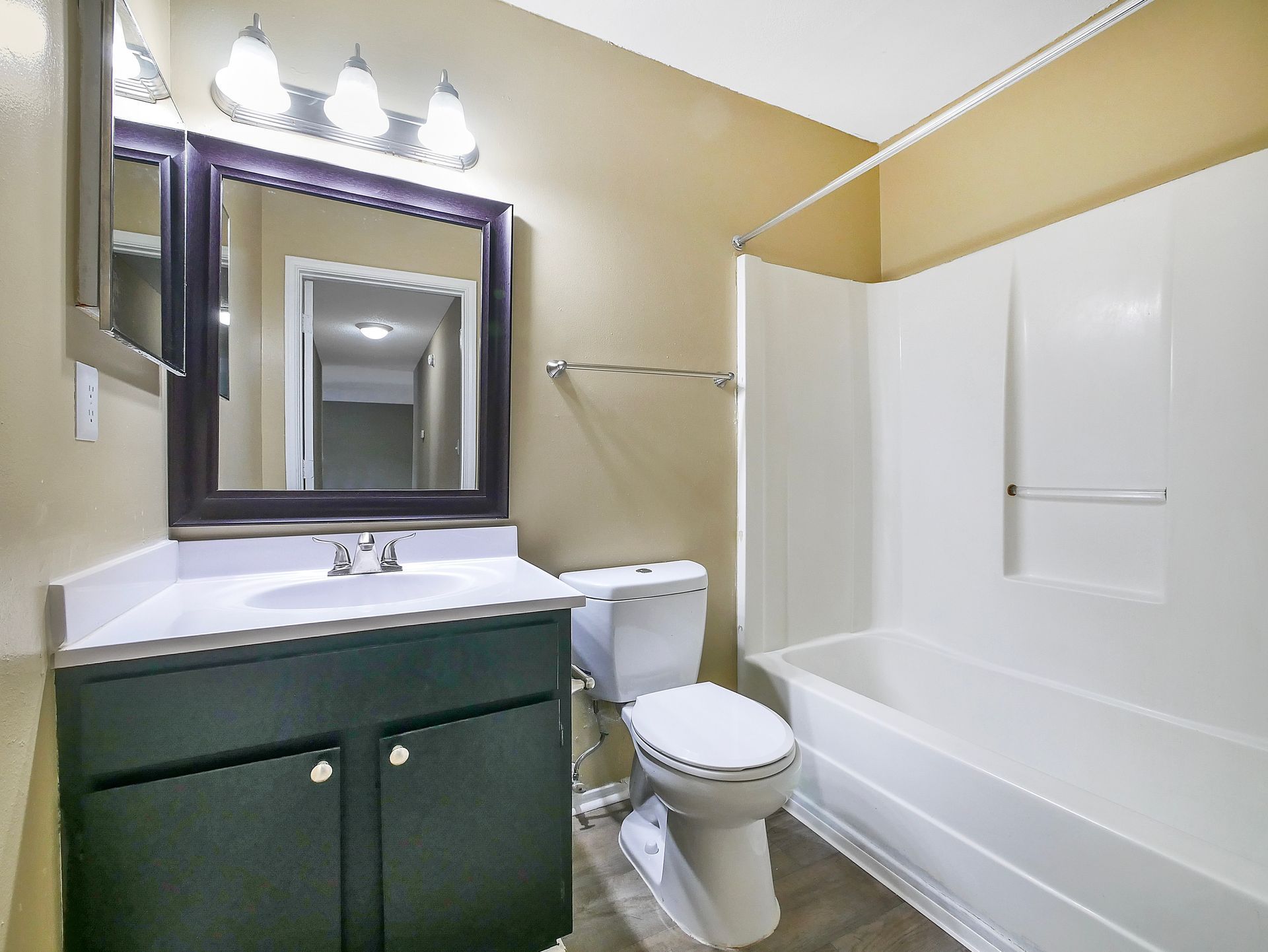 A bathroom featuring a dark vanity with a white sink, a mirror with a dark frame, a toilet, and a white shower-tub unit.