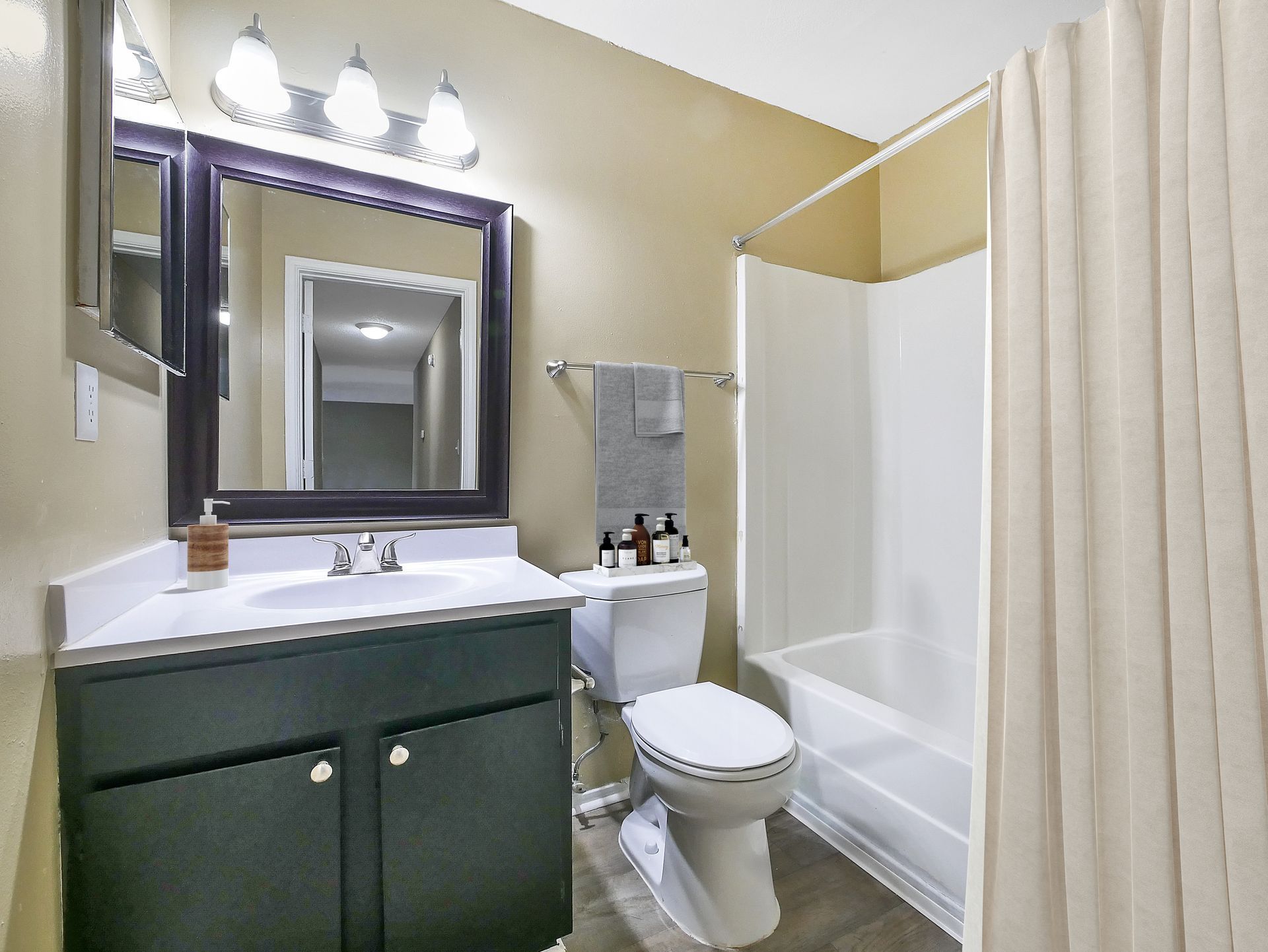A bathroom with a dark vanity, white sink, mirror, toilet, and a bathtub with a beige shower curtain.