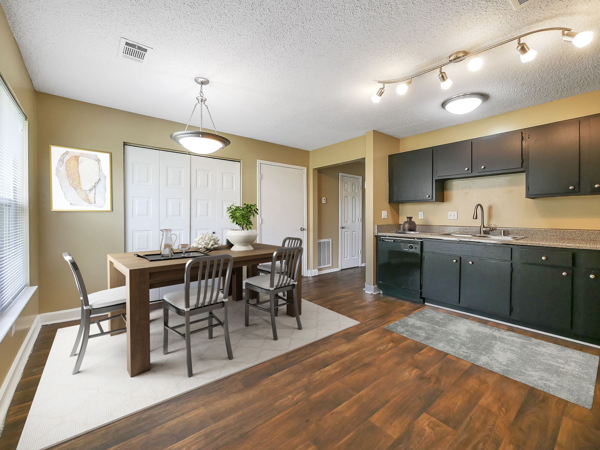 A kitchen and dining area featuring a wooden dining table with four chairs and dark cabinetry against a tan wall.