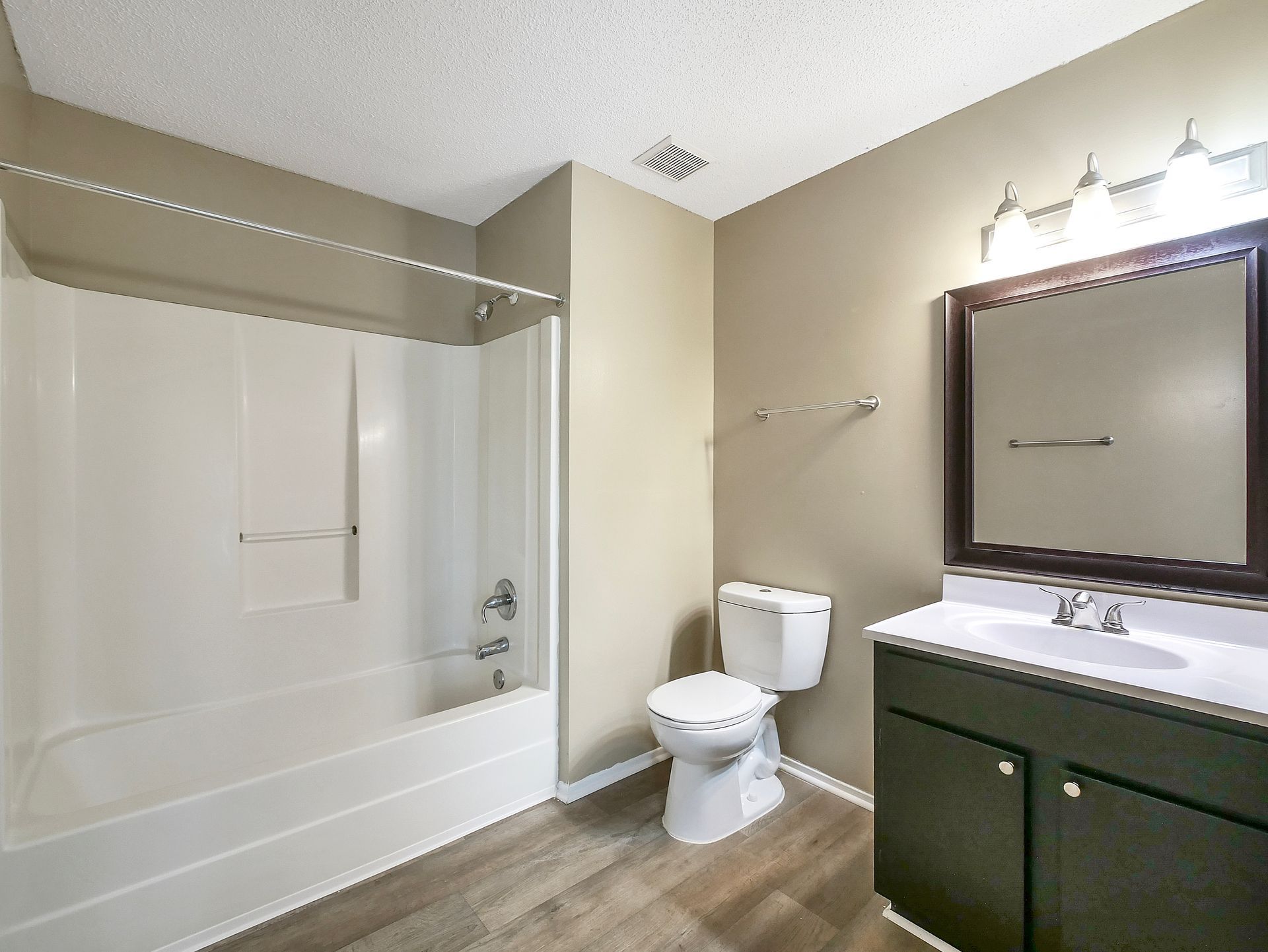 A bathroom with a white bathtub and shower unit, a toilet, and a vanity cabinet with a mirror and light fixture.