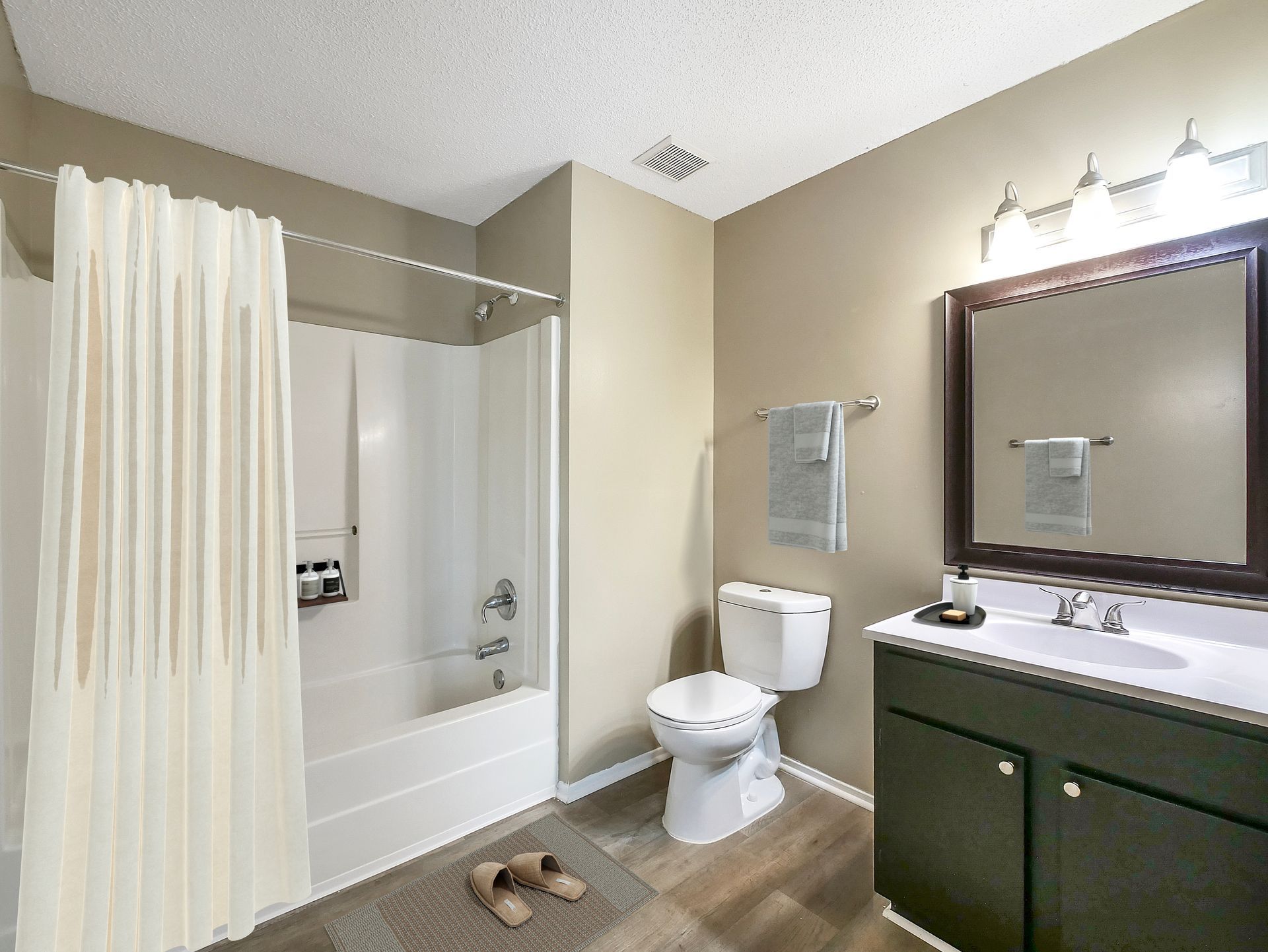 A bathroom with a white shower curtain, bathtub, toilet, and a vanity with a dark cabinet and mirror.