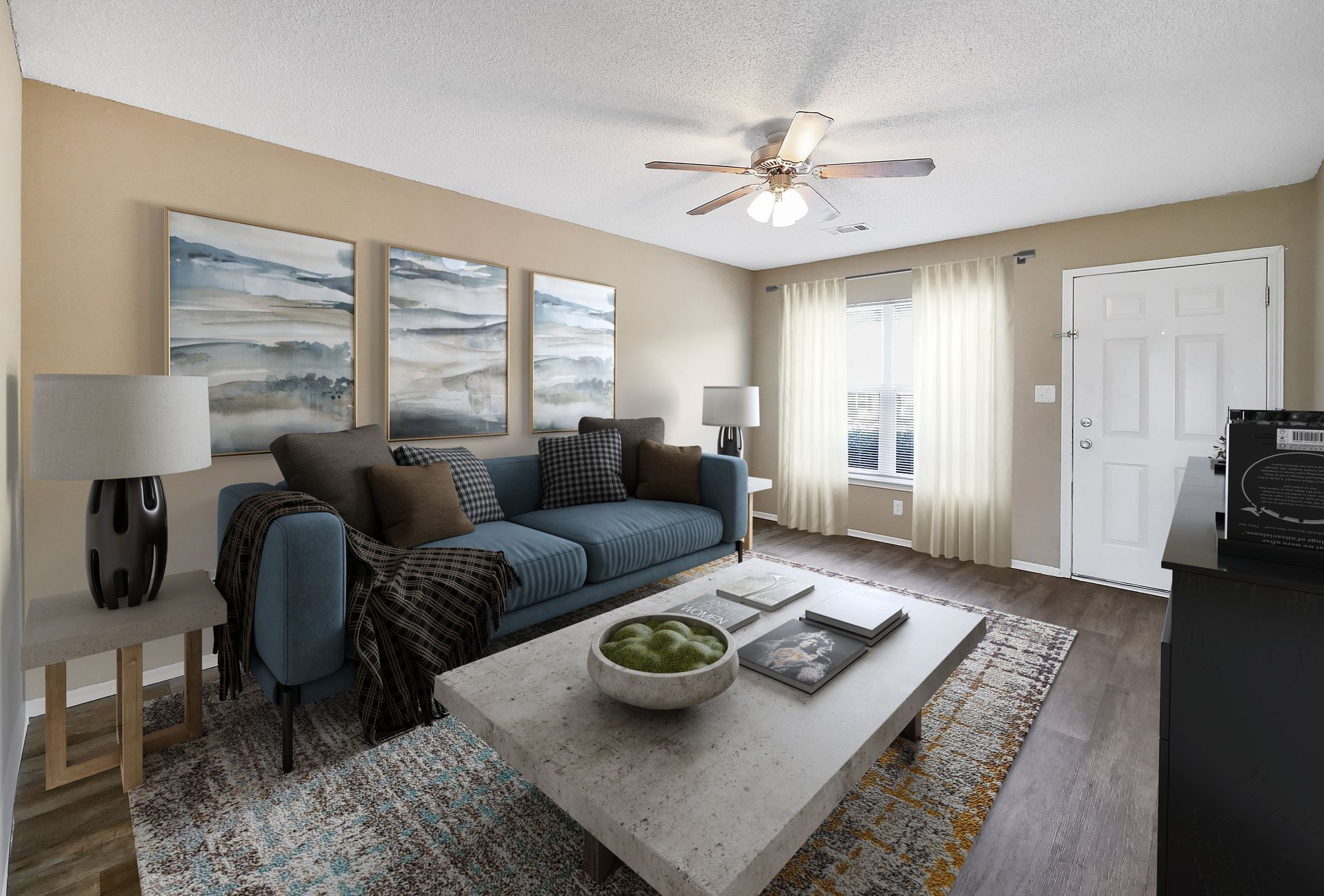 A modern living room with a blue sofa, light wood end table, concrete coffee table, and three abstract wall art pieces.